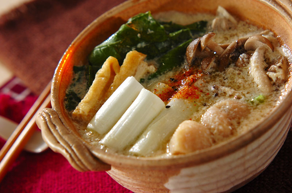 土鍋で煮込まれている鶏肉やきのこ、小松菜などの豆乳鍋