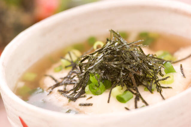 白い丼鉢に盛りつけられたそば米と鶏肉、刻み海苔入りのとろろ汁
