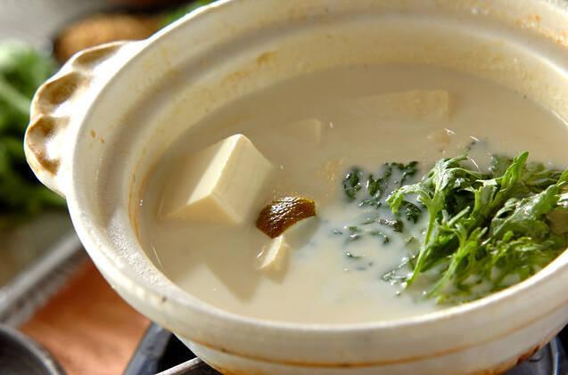 白い土鍋に入っている豆乳みそスープと春菊、ゆずの皮の湯豆腐