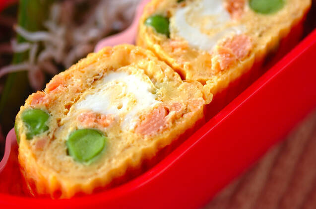 赤いお弁当に盛りつけられたグリーンピースと鮭のだし巻き卵