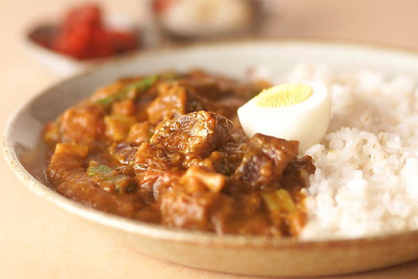 グレーの皿に盛り付けたサバと野菜のカレー、ゆで卵