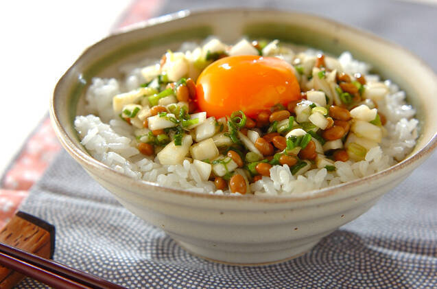 白い椀に盛り付けられた新玉ねぎ入り納豆丼に卵黄がトッピングされている