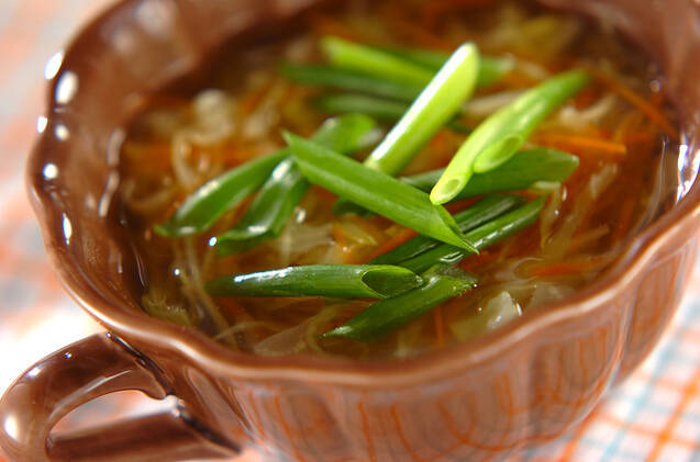 茶色のコップ型の器に入っているキャベツとニンジンのノンオイルコンソメスープがカラフルなランチョンマットの上に置いてある