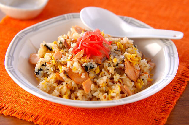 赤いランチマットの上にある、中華皿に盛り付けられ紅ショウガをトッピングされたた鮭チャーハン。