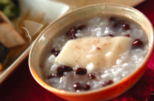 朱色の茶碗に盛りつけられている、餅と小豆入りのお粥