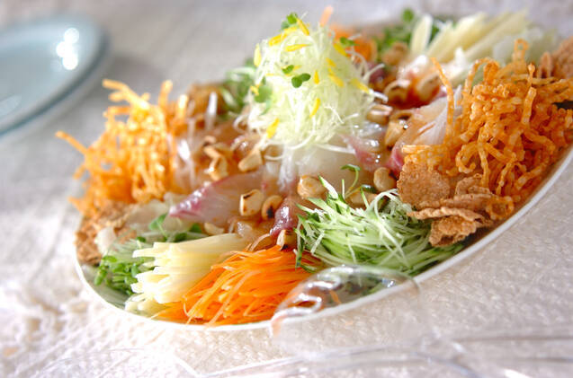 にんじん、きゅうりなどの色とりどりの野菜と刺身、コーンフレークがのったコーンフレーク入りお魚サラダが白いお皿に盛ってある