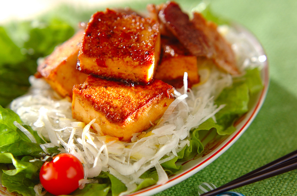 サラダの上に豆腐と豚バラ肉の中華炒めが盛られている様子