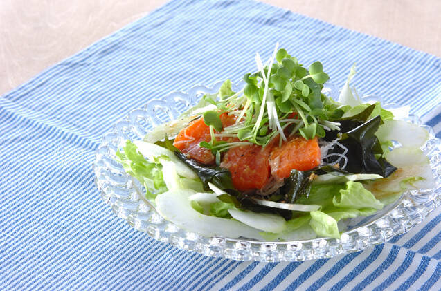 ガラスの丸皿にサーモンとわかめのサラダが盛られ、青いストライプ模様のランチョンマットを敷いた机の上に置かれている
