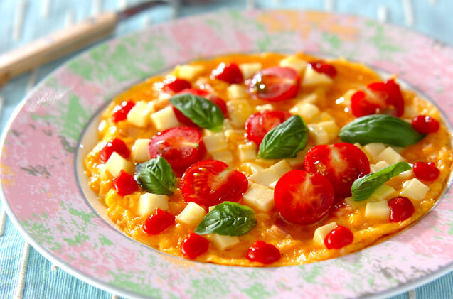 模様入りの皿に盛りつけられたミニトマトとチーズ入りのオムレツ
