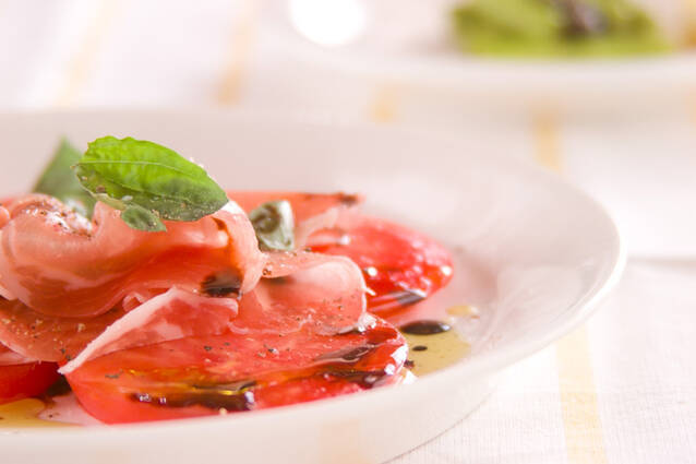 白い皿に盛りつけられた生ハムとトマト、バジルのカルパッチョ風