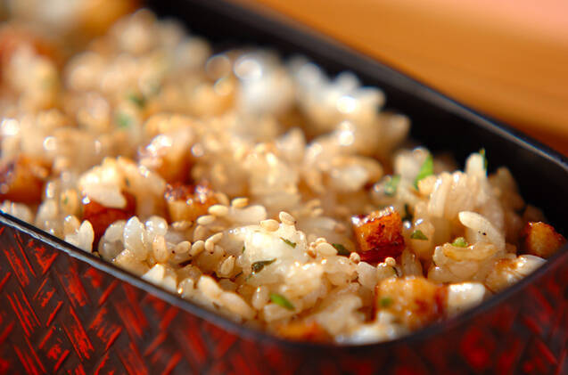 赤い模様入りのお弁当箱に盛られ、白いりごまをトッピングした蒲焼きちくわと大葉の混ぜごはん