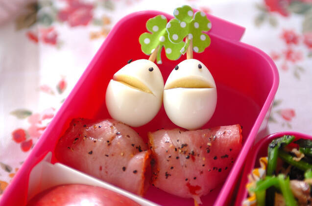 ピンクのお弁当箱の中のうずら顔つきプチトマトのベーコン巻き