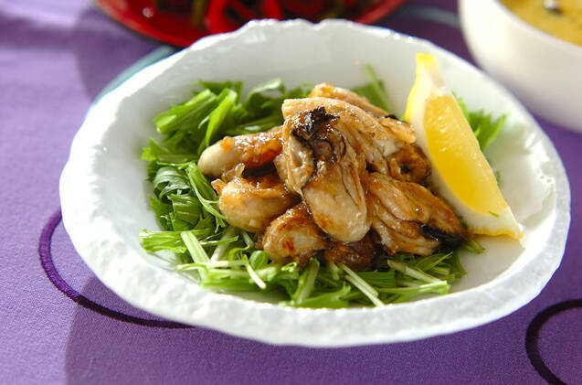 白い器に水菜とカキの揚げ焼き、レモンひと切れが盛られている様子