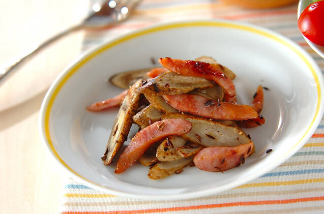 黄色い縁取りの白い楕円の皿に盛られたごぼうとソーセージの炒め物