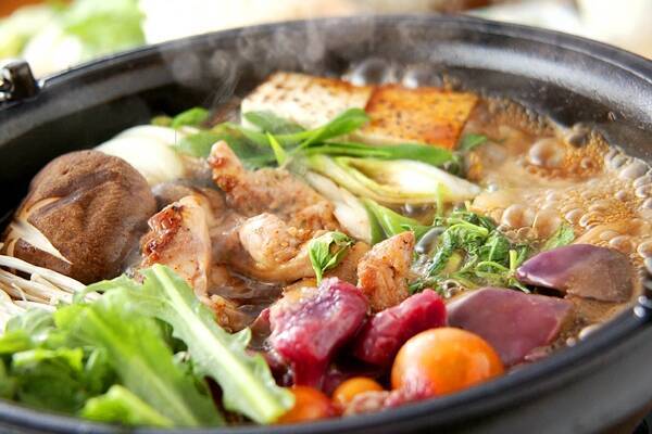 黒い鉄鍋に入っている鶏もも肉や野菜、鶏もつなどのすき焼き