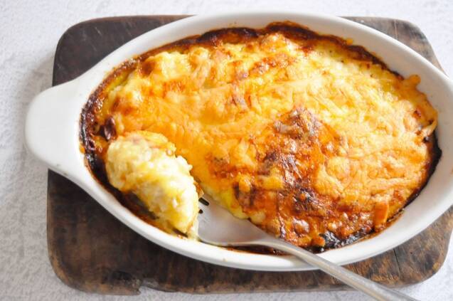 白い耐熱容器に盛られたグラタンをスプーンですくっている様子