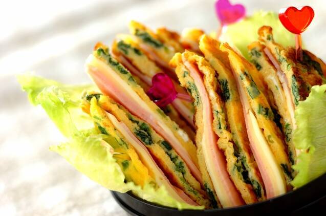 黒い弁当箱に盛りつけられた、ハムとチーズのサンドイッチ風卵焼き