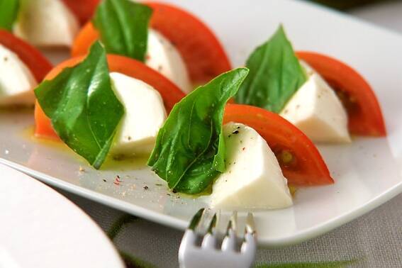 スライスしたトマトとモッツァレラチーズ、バジルのカプレーゼが白い皿に美しく並べられているところ