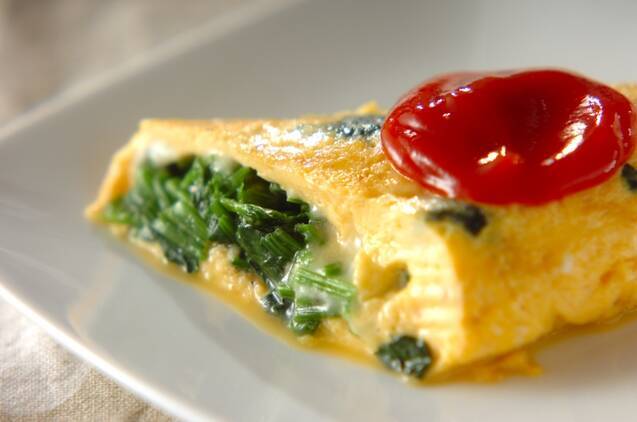 白いプレートに盛り付けた半分にカットしたほうれん草入りチーズオムレツ