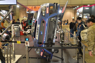 クルマが横倒しでマフラーまる見え！　フジツボブースの展示は技術力もまる見えだった【東京オートサロン2026】