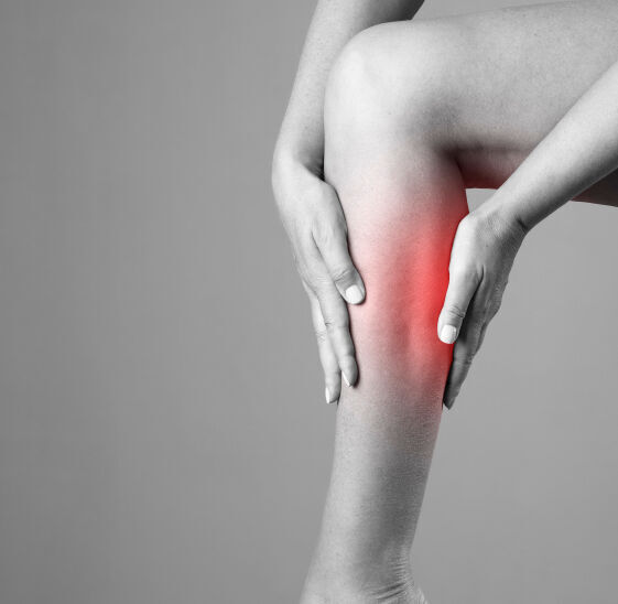 Pain in the calf muscle of the woman. Massage of female feet. Pain in the human body on a gray background