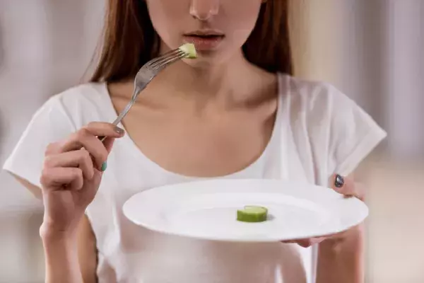 皿の上のひとかけらの野菜を口に運ぶ女性