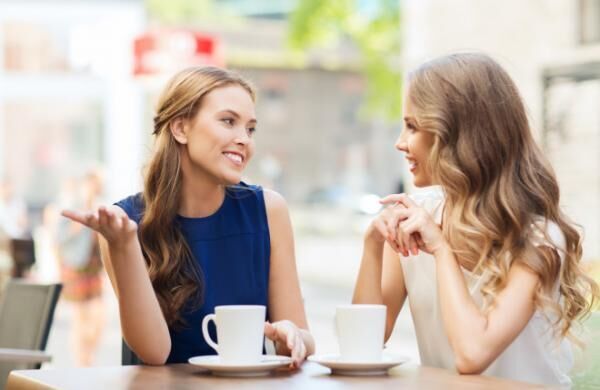 young women drinking coffee and talking at cafe