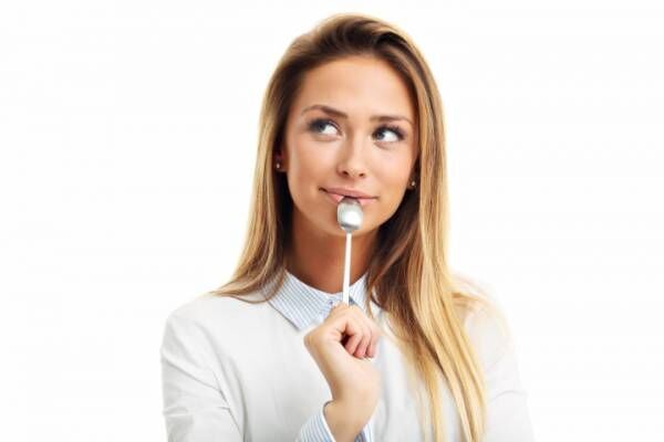 Portrait of young smiling woman with spoon in her mouth isolated on white