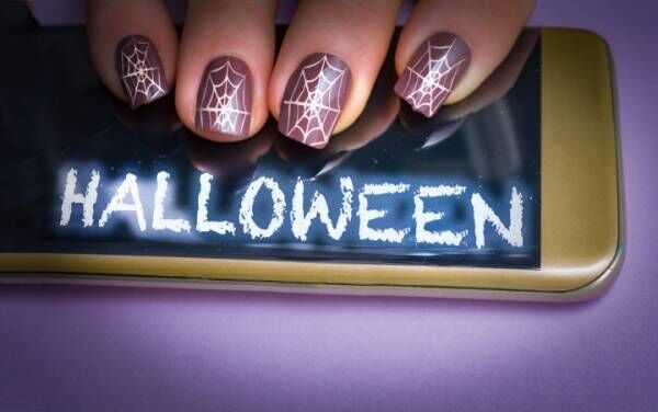 Woman with halloween cobweb nails on her glowing smartphone