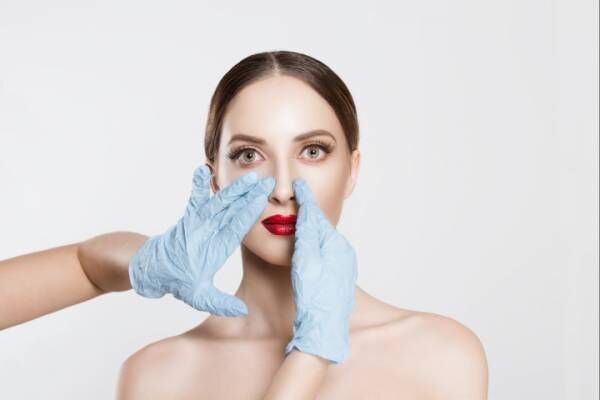 Rhinoplasty. wish to be beautiful need for beauty. Closeup portrait doctor hands with gloves touching woman face nose want to change her form do plastic surgery. cropped image horizontal studio shot