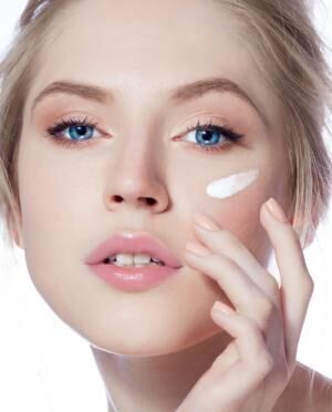 Portrait of young woman applying moisturizer cream