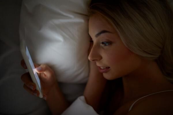 young woman with smartphone in bed at home bedroom
