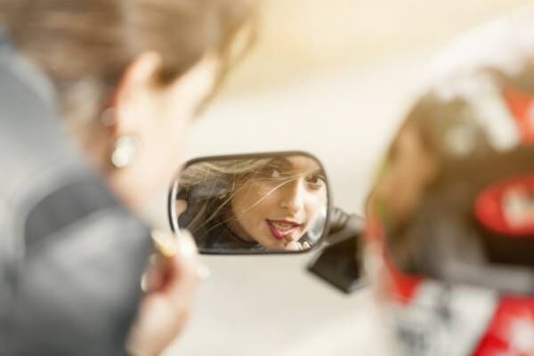 Beautiful woman on motorcycle mirror fixing make up