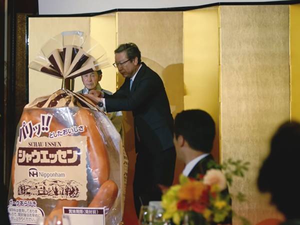 『巨大シャウエッセン』を囲む人々　謎の披露パーティに「お腹抱えて笑った」