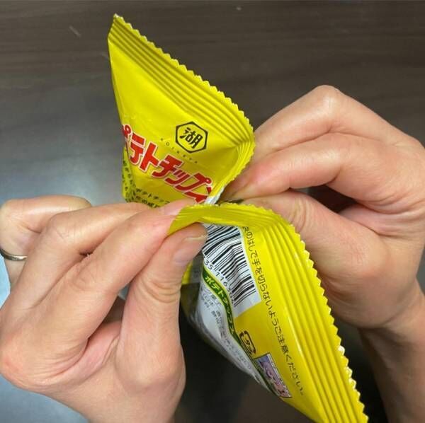 袋の上から両手で開けようとしているポテトチップスの袋