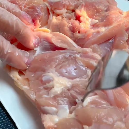 鶏もも肉を包丁で切っている