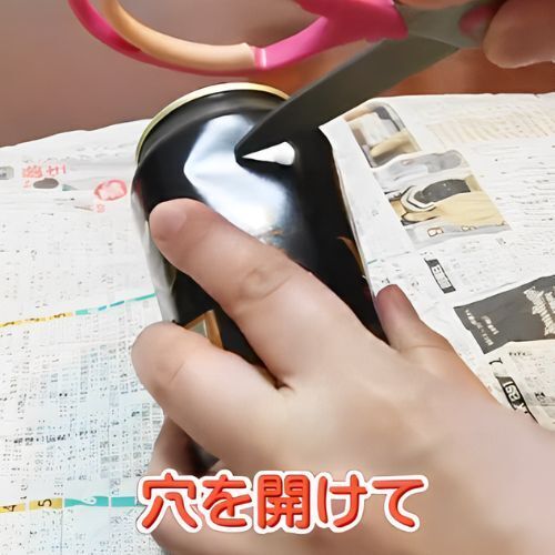 新聞紙の上でアルミ缶にハサミで穴を開ける様子