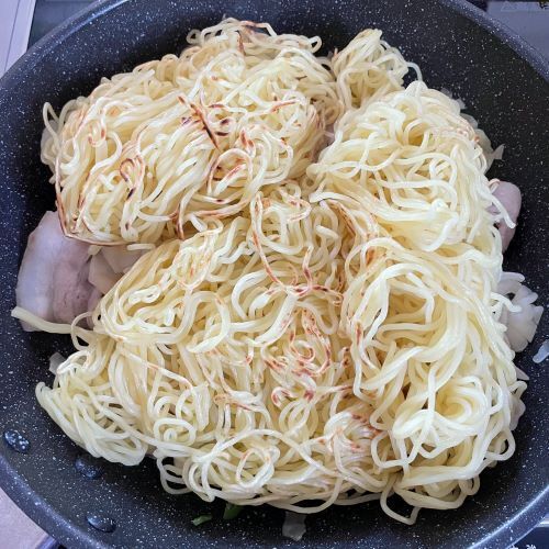 炒めた具材に事前に焼き目を付けた麺を入れた様子