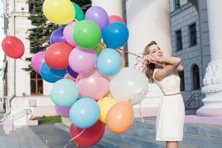 15574973 - happy young woman with colorful latex balloons keeping her dress, urban scene, outdoors