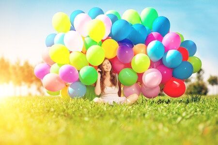 30750674 - happy birthday woman against the sky with rainbow-colored air balloons in her hands. sunny and positive energy of nature. young beautiful girl on the grass in the park.