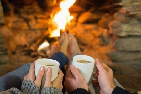 25460005 - close up of hands holding coffee cups in front of lit fireplace