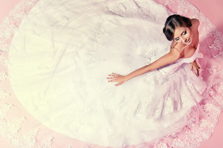 24063770 - beautiful charming bride in a luxurious dress looking up. over pink background.