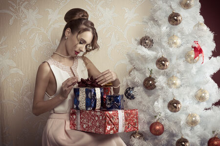 47726886 - elegant beautiful woman with hair-style sitting near decorated tree with some christmas presents. xmas concept.