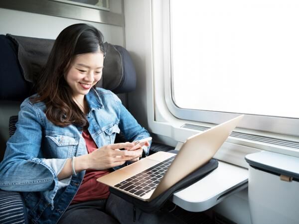 Asian woman smiling at smartphone with laptop on train