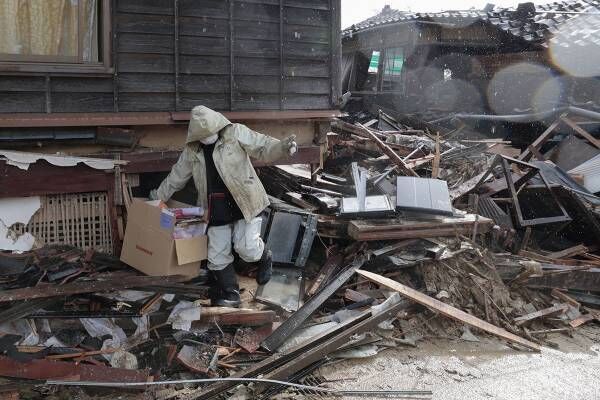 能登町にて倒壊した自宅から荷物を運び出す女性（写真：共同通信）