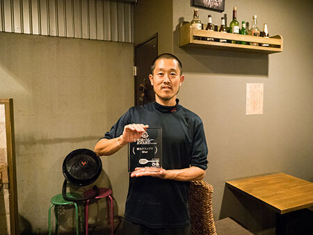 「第4回 究極のカレーAWARD」総合GPを記念した盾が手渡され、喜びをかみしめる「Ghar」店主の鈴木さん。