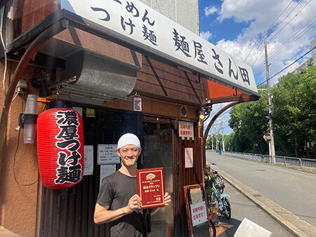 総合グランプリを記念した盾を手渡され、店前で受賞の喜びをかみしめる「麺屋 さん田」店主の三田さん。